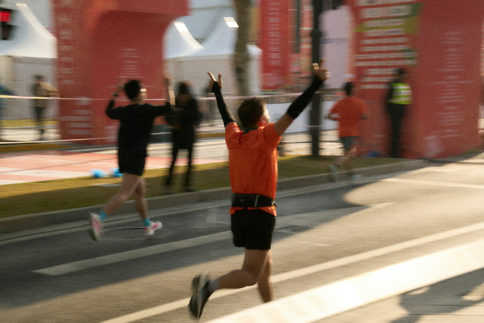 A runner crossing a road-race finish line with arms raised